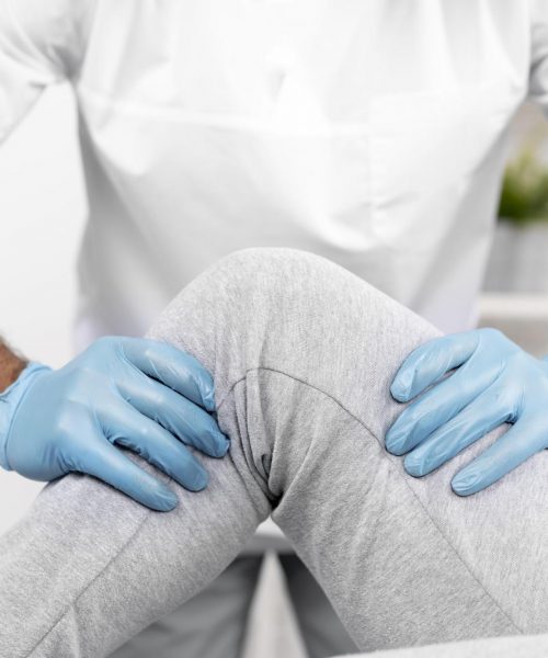 Massage therapist with blue gloves adjusting knee in gray sweatpants